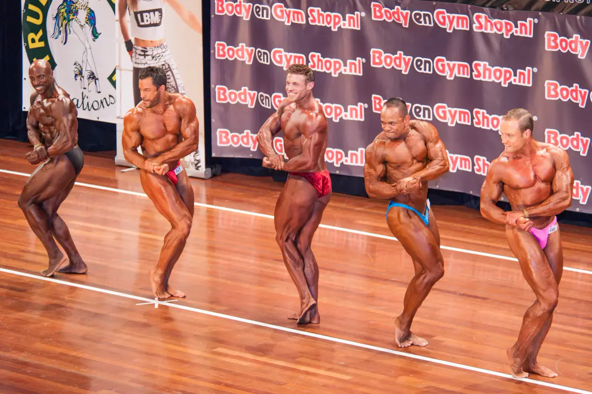 Male bodybuilders hitting poses in a lineup on a competition stage