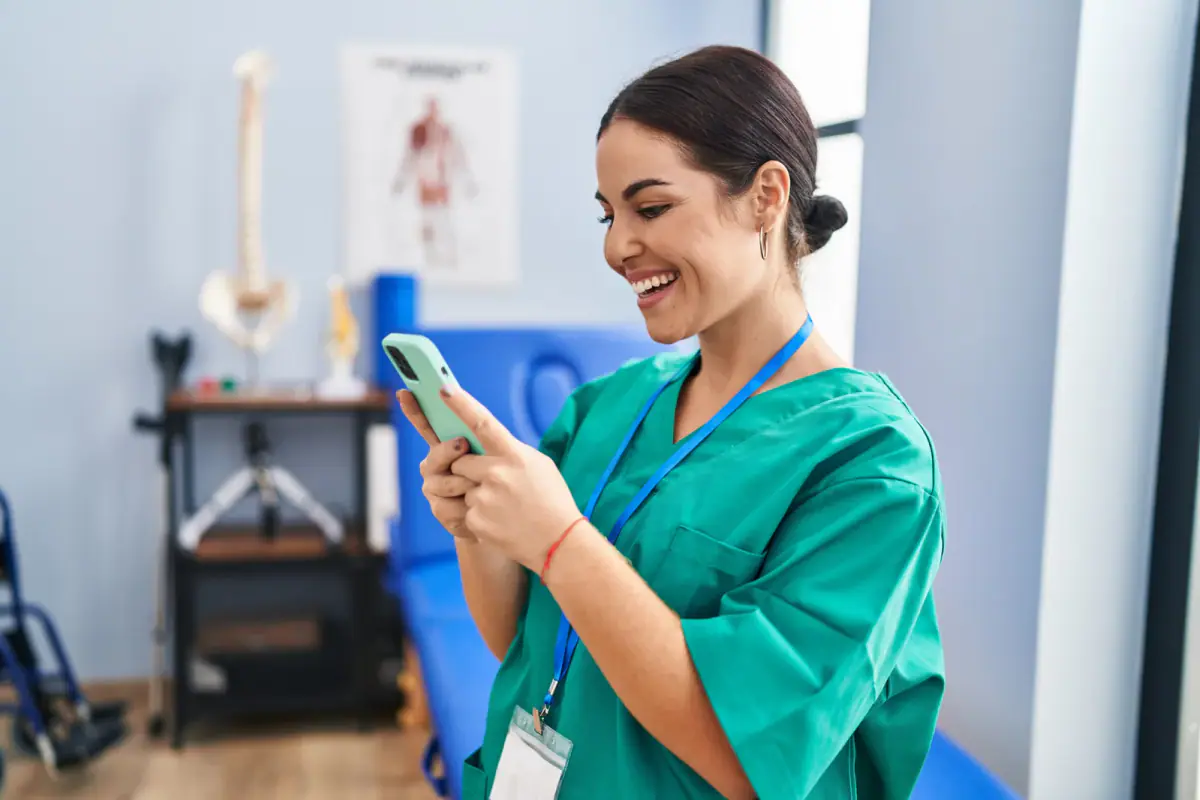 A smiling woman physiotherapist using a smartphone at a rehab clinic, relevant to a portable table in a rented room