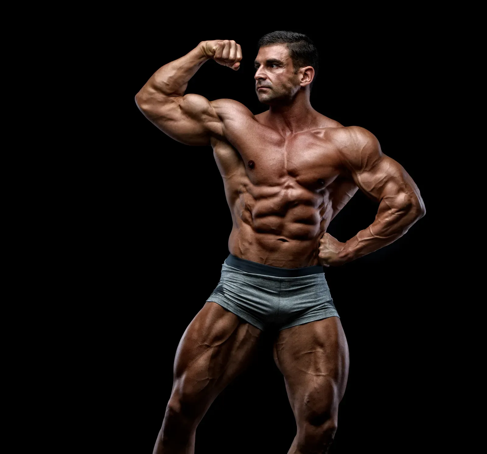 Physique competitor rehearsing a posing routine under low lighting