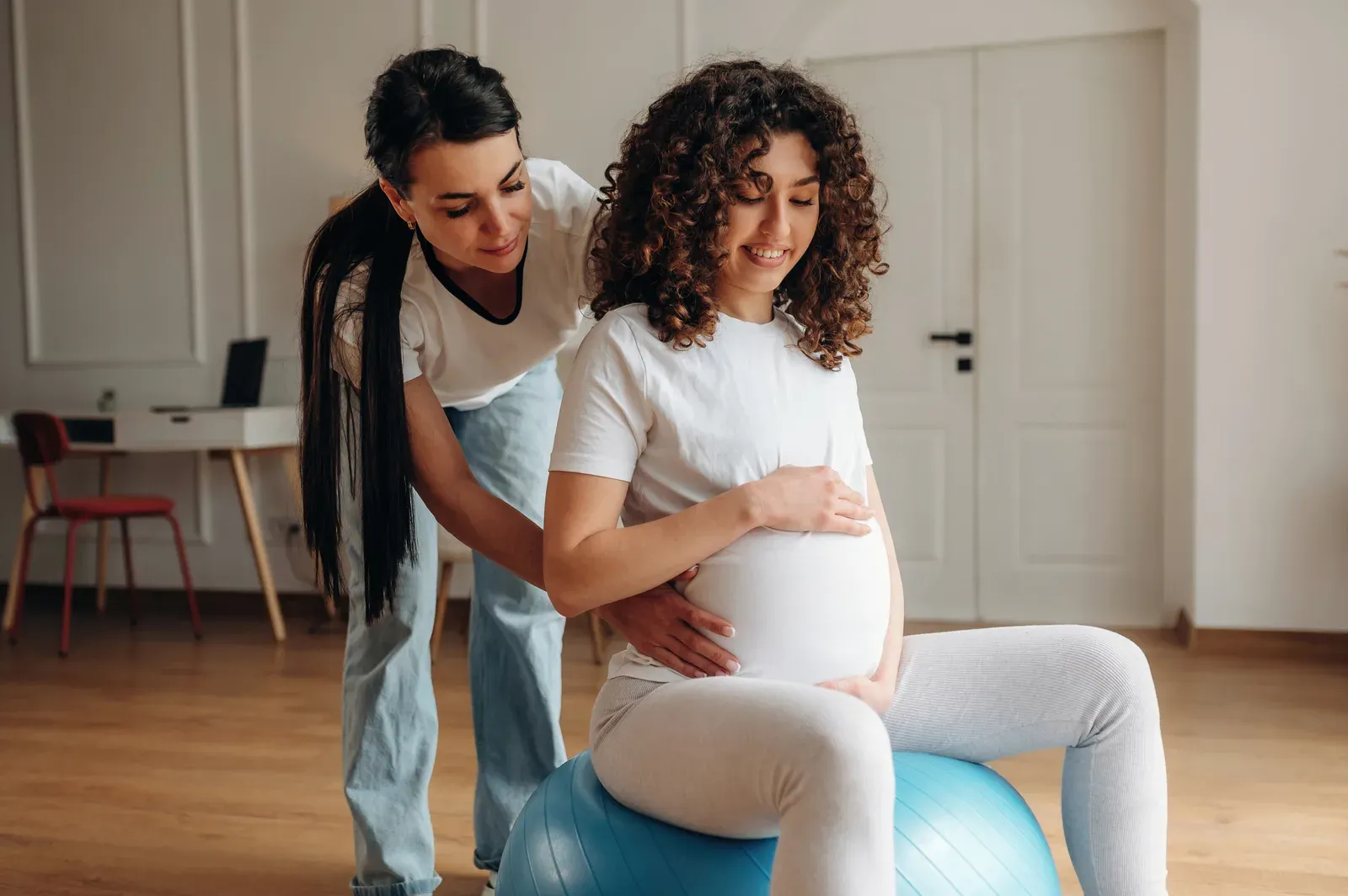 Pregnant woman balancing on an exercise ball with support from her instructor