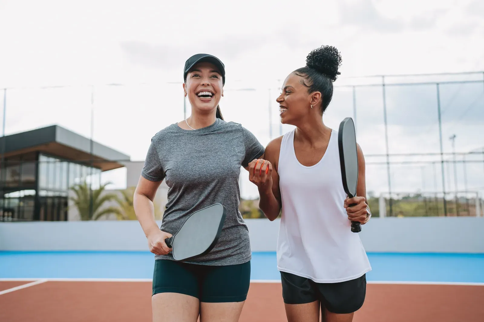 Two smiling women with pickleball paddles walking off an outdoor court