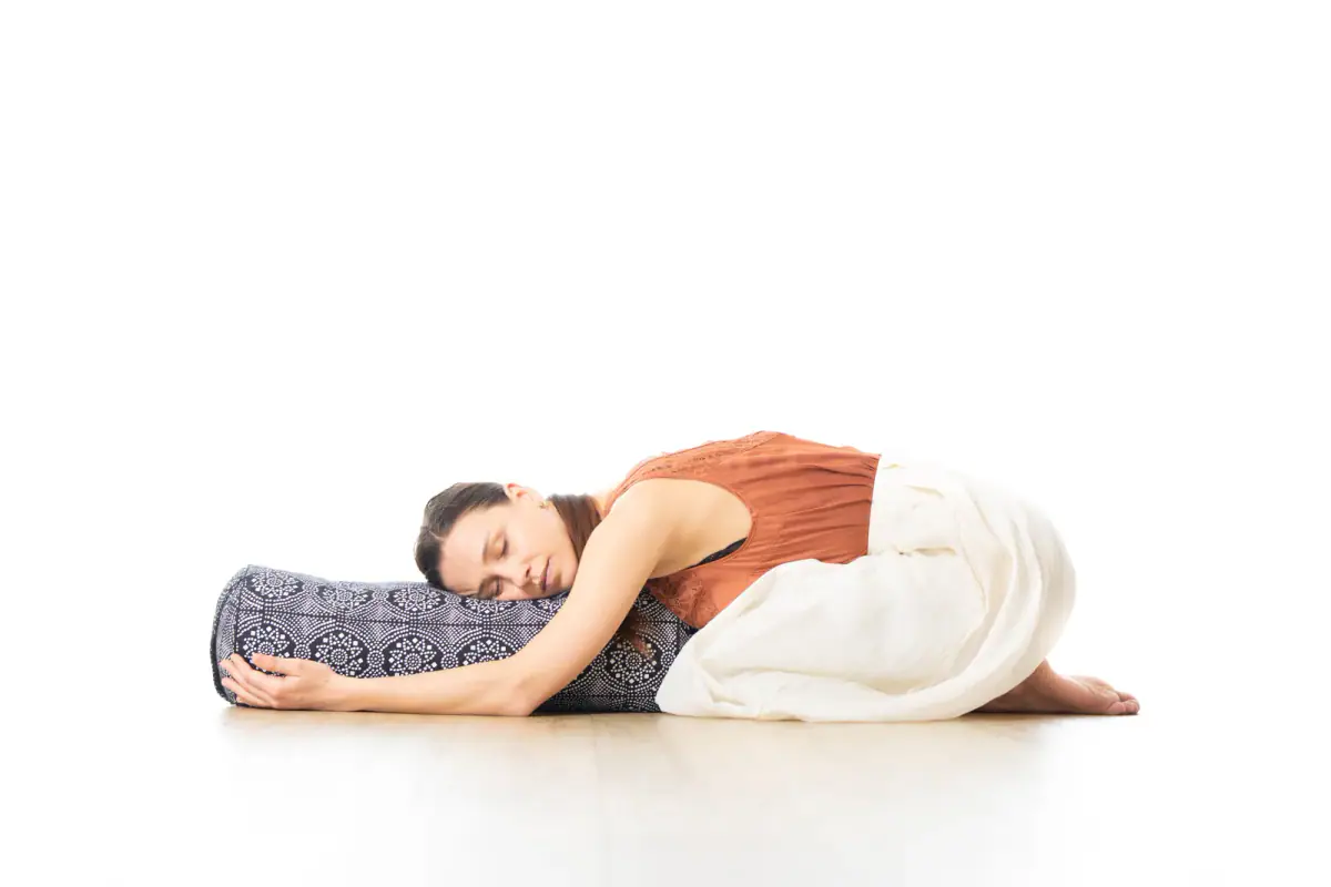 A woman doing restorative yoga on a bolster in a bright white studio, relevant to setting up a private room