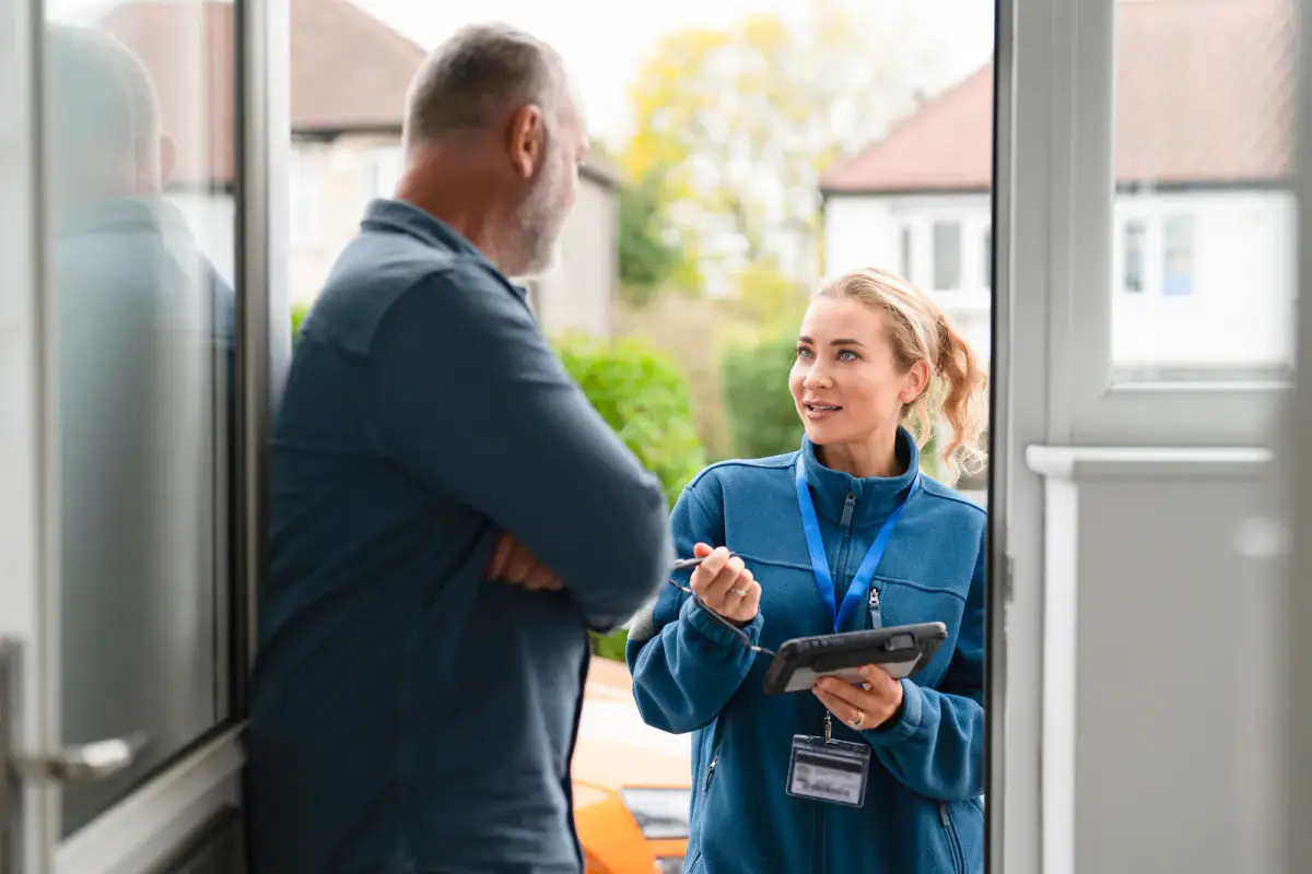 A service professional discussing options with a homeowner at a house entrance on a sunny day, like trainer safety at client homes