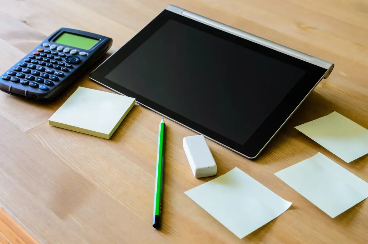 A workplace with a tablet, calculator, pencil and sticky notes, relevant to saving before going independent as a trainer