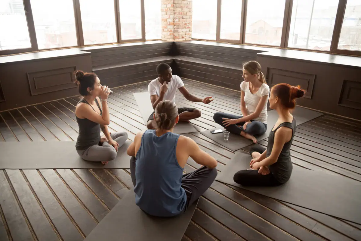 Yoga instructor talking with a group of students seated on mats