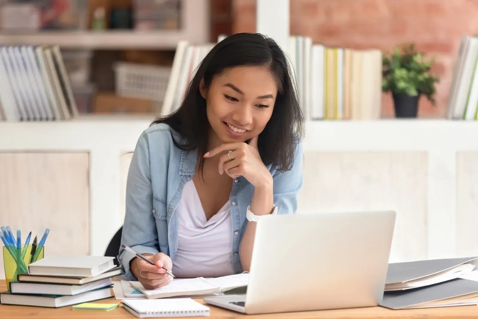 Laptop and books open in a library as a student studies with a smile