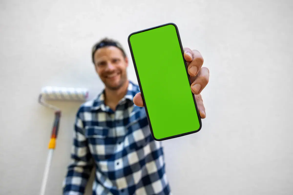 A man showing a smartphone with a green screen for online service booking, relevant to clients self booking sessions