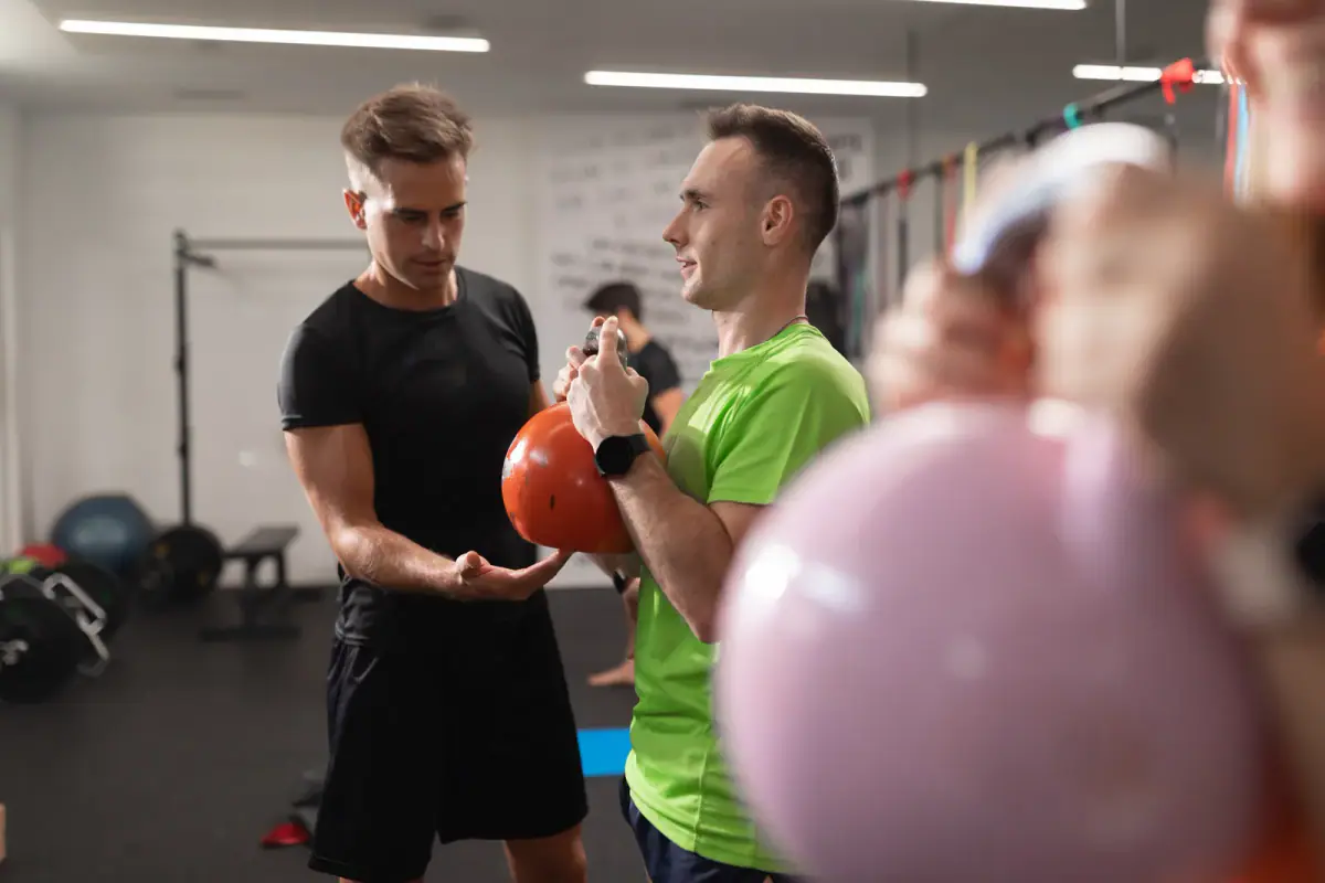 A trainer assisting a trainee performing squats with a kettlebell, relevant to small group training price per person
