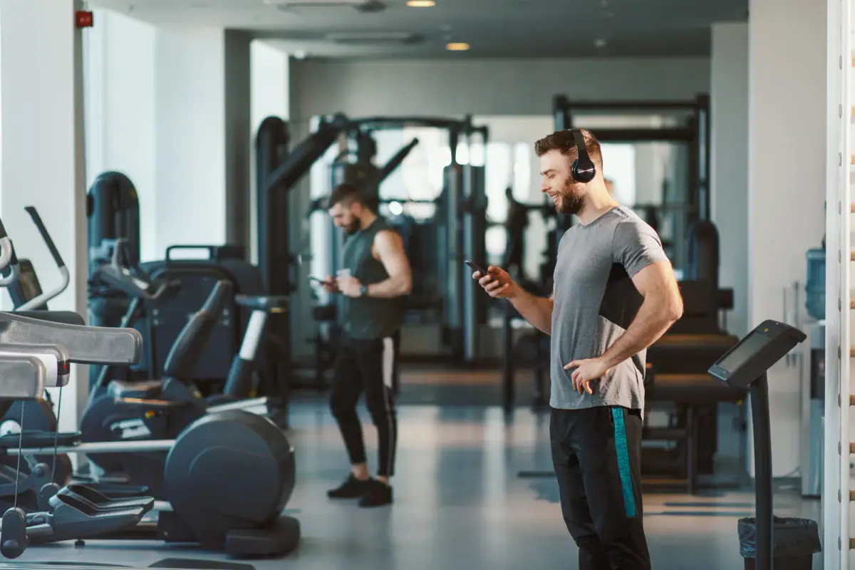 A young man choosing music on a smartphone as he prepares to work out, relevant to sound in a rented training room