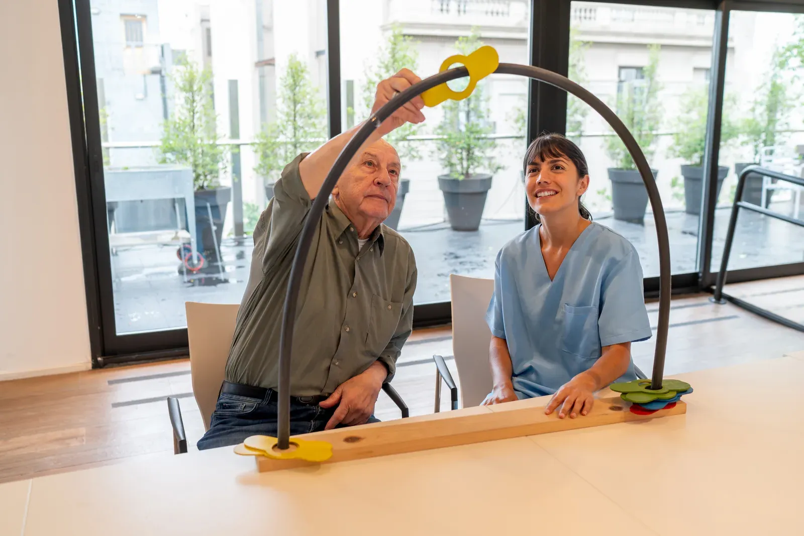 An occupational therapist guiding a senior man through a tabletop arch and ring coordination exercise