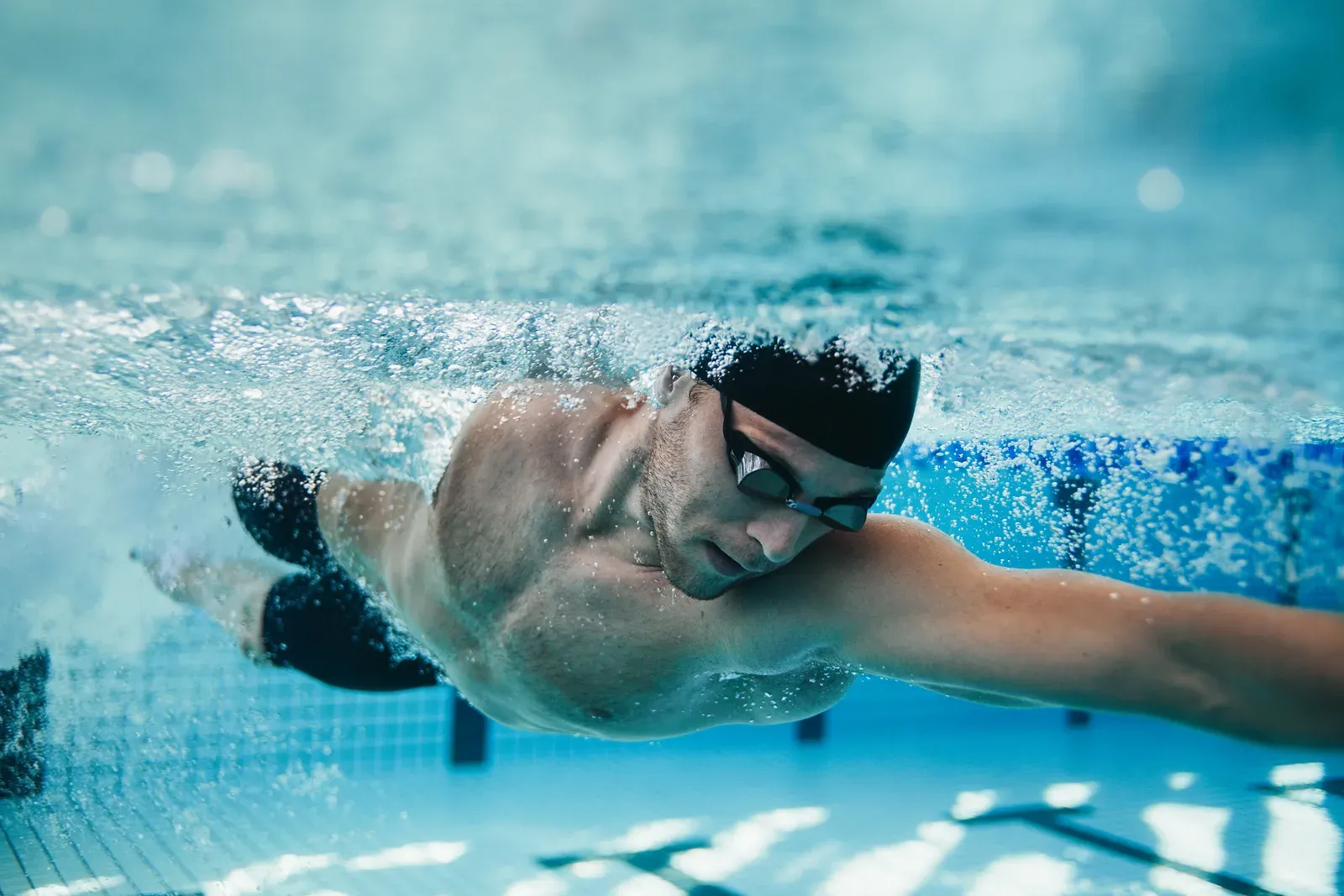 An underwater view of a swimmer in cap and goggles swimming freestyle