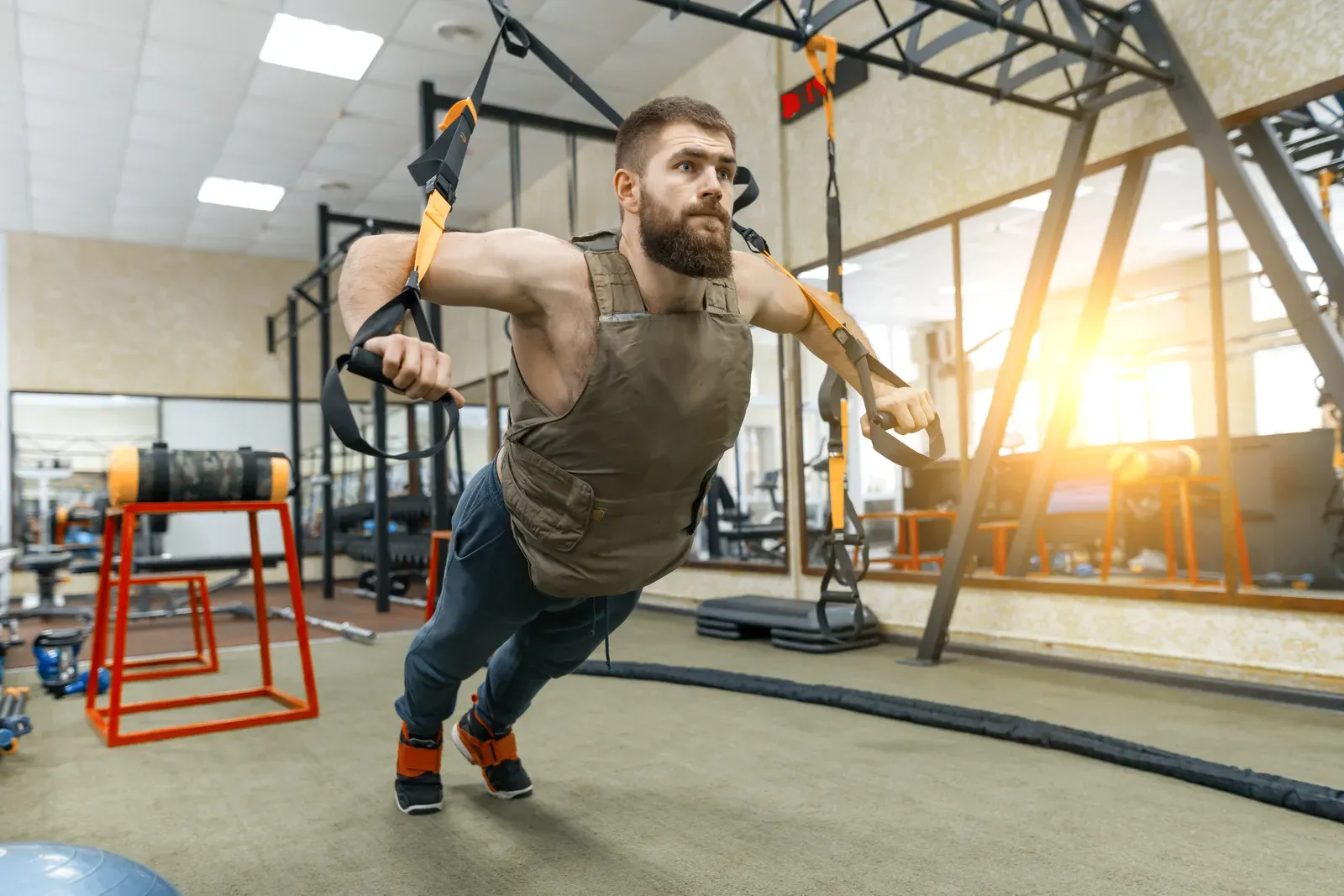 A man in a weighted vest doing suspension trainer exercises in a gym