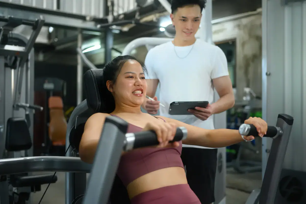A determined woman doing a chest press guided by her personal trainer, relevant to telling clients you are leaving the gym
