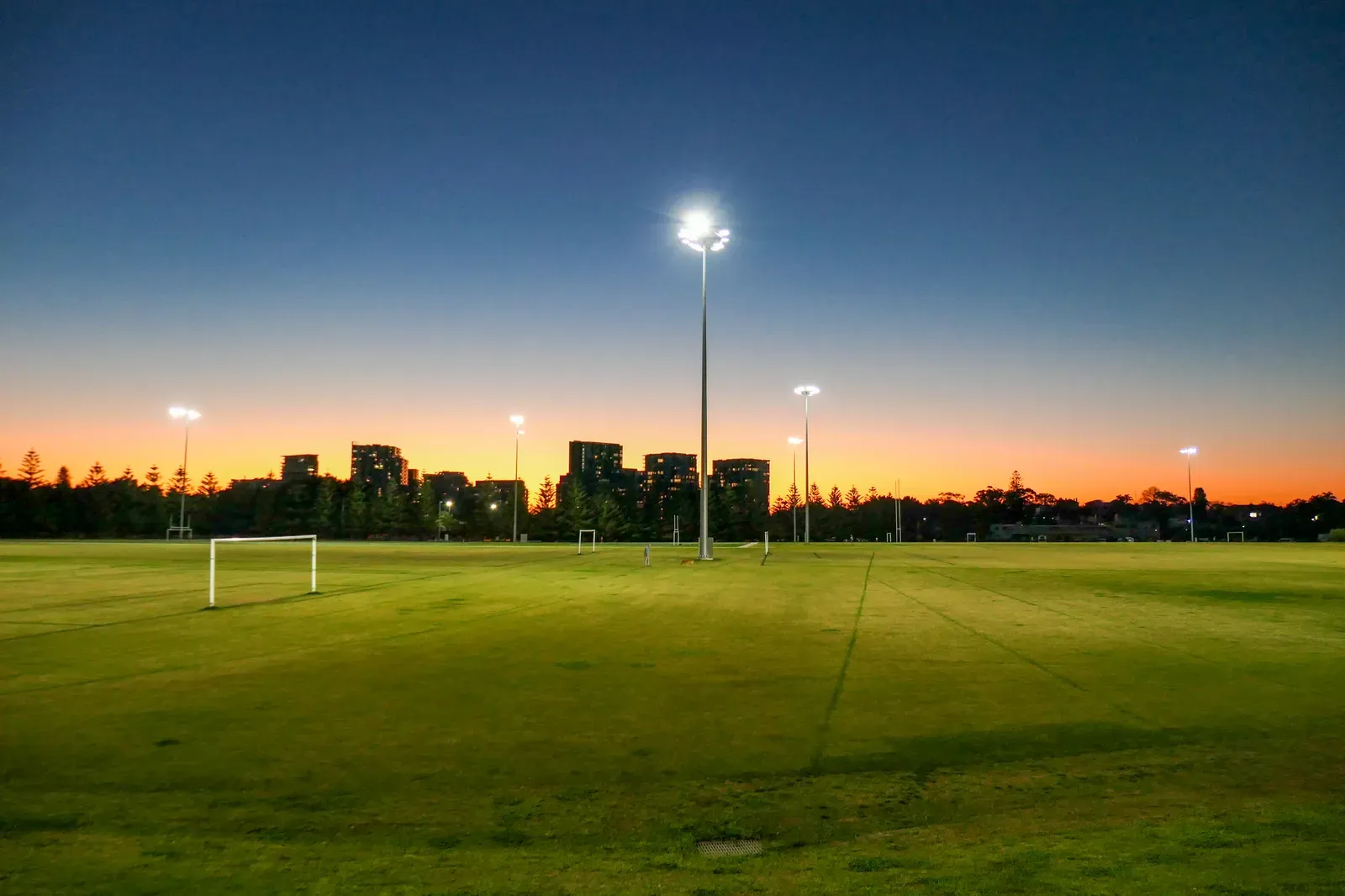 Floodlit grass sports fields at dusk with goals and light towers