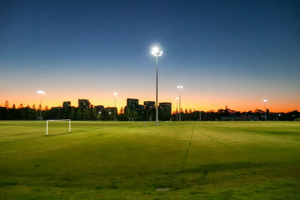 Floodlit grass sports fields at dusk with goals and light towers