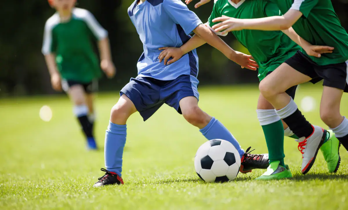 Youth soccer players in blue and green uniforms challenging for the ball