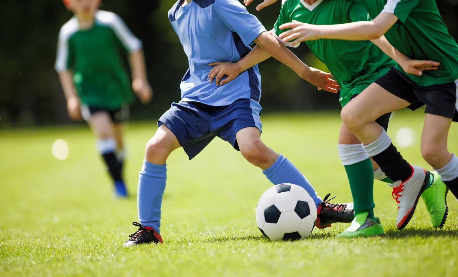 Youth soccer players in blue and green uniforms challenging for the ball