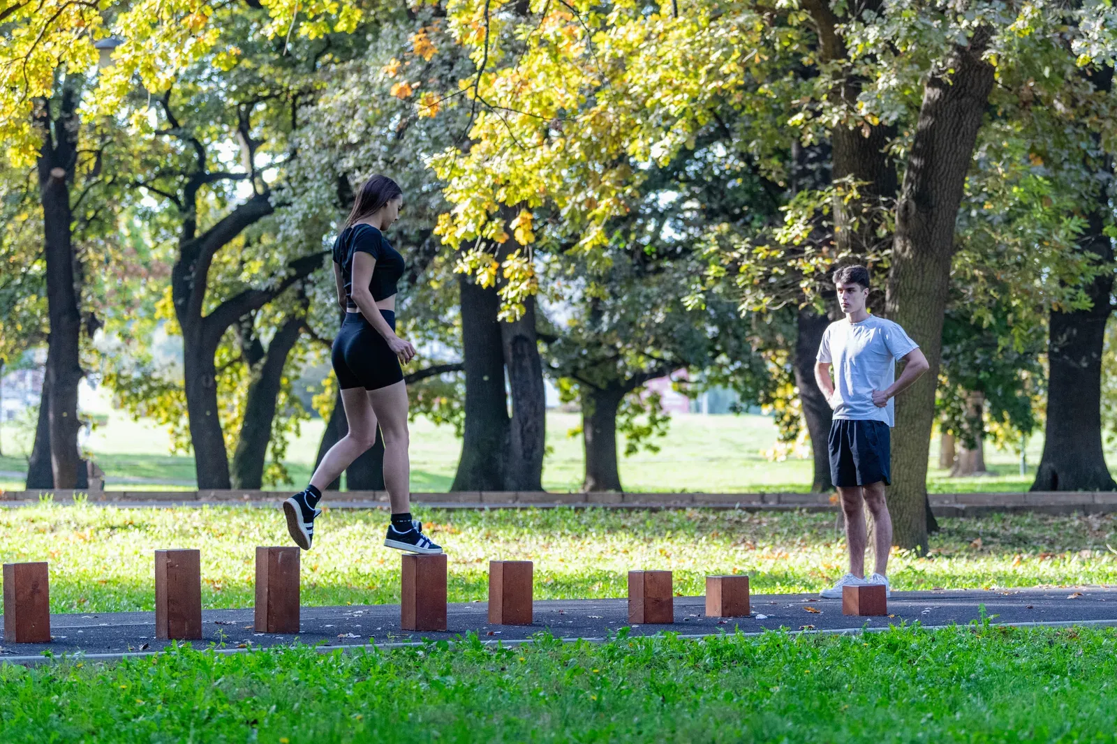 Outdoor park workout on wooden hurdles, a couple training balance and coordination