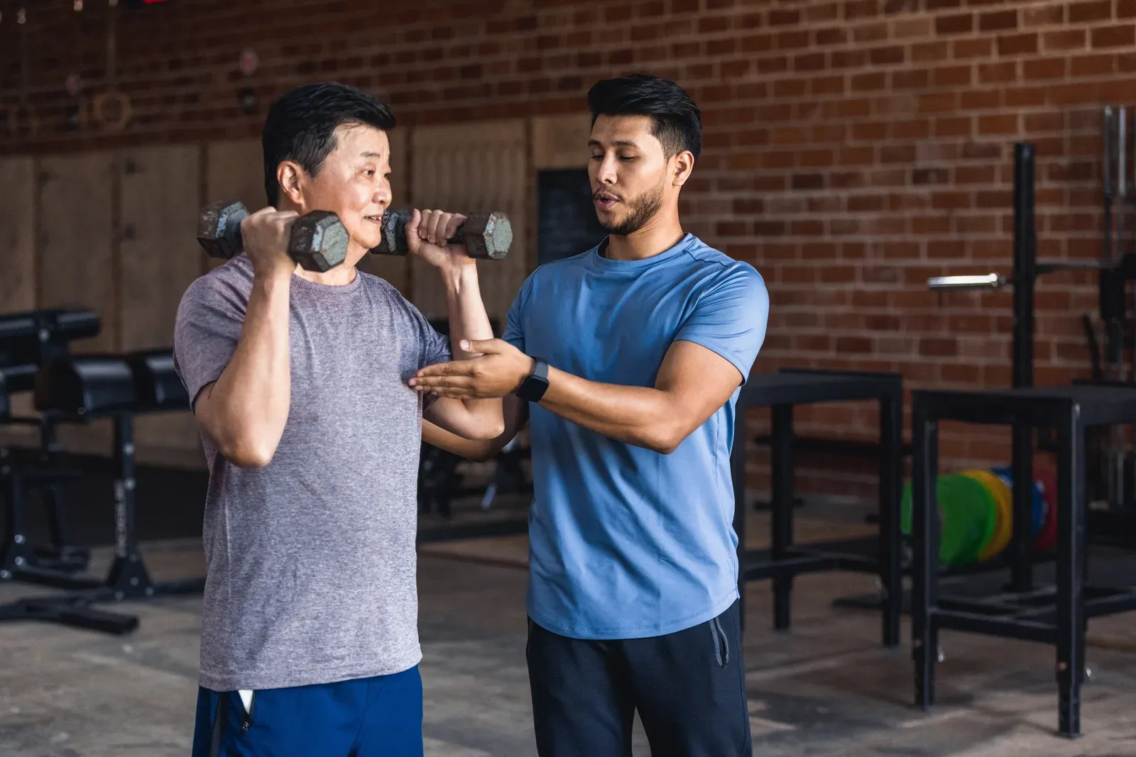 A trainer guiding a middle aged client through a dumbbell exercise