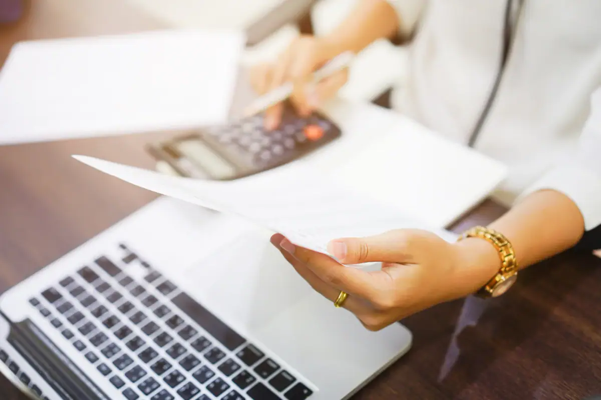 Employee holding a statement report and pressing a calculator, a step in finding a true hourly rate for an independent trainer