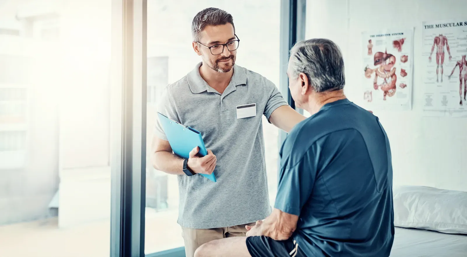 A chiropractor with a clipboard consulting a senior patient in a treatment room