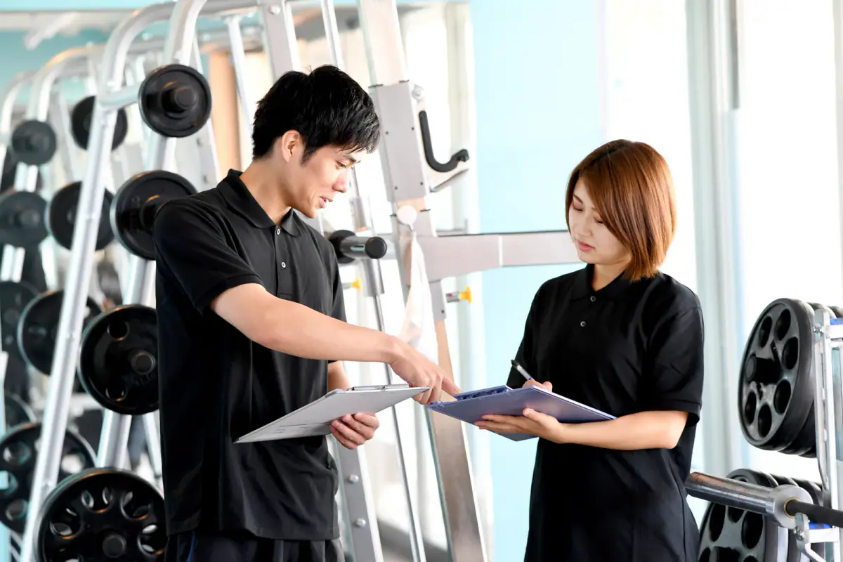 A young male and female fitness instructor having a conversation at the gym, relevant to when to hire a second trainer