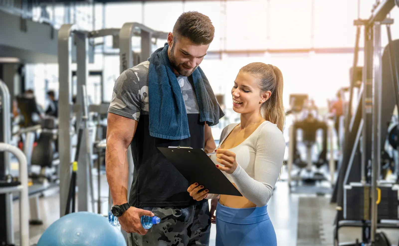 Trainer and client going over a workout plan together on a busy gym floor