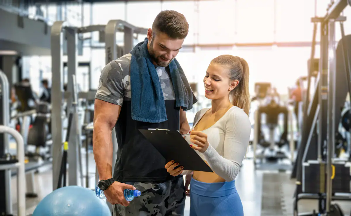 Young female personal trainer showing exercise progress to a male client in the gym, a client base to carry into going independent