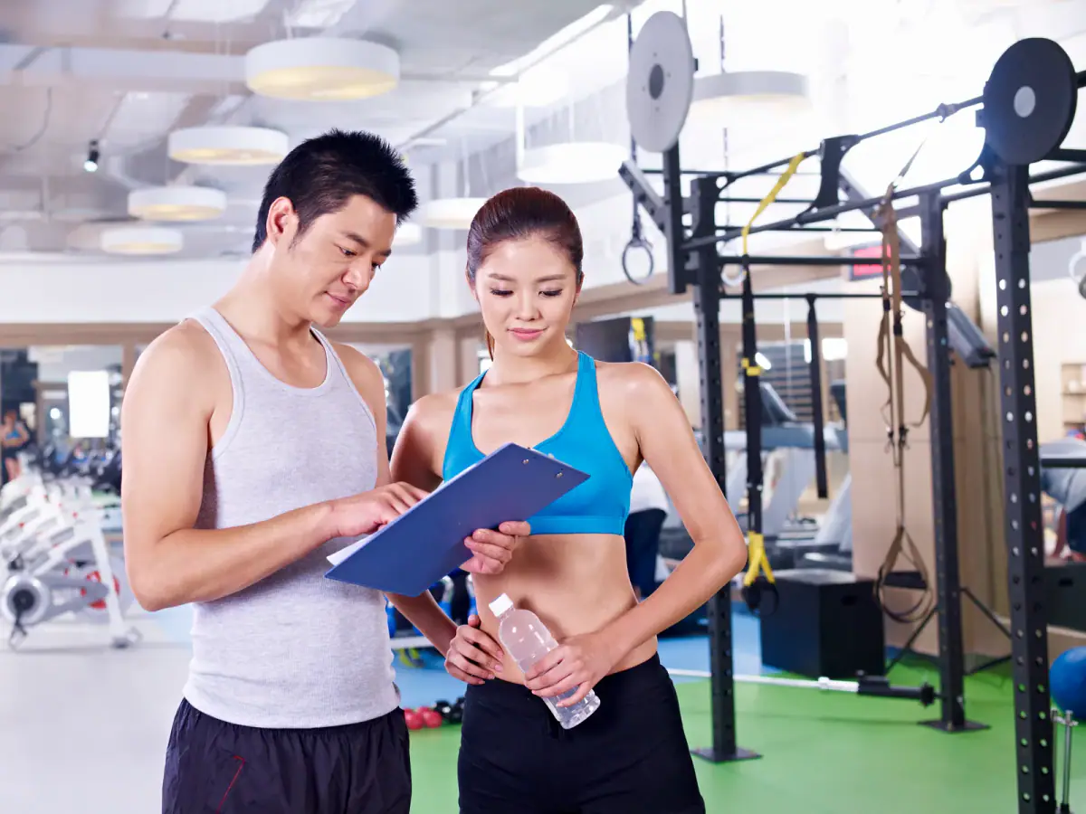 Coach and client checking a printed program together next to gym equipment