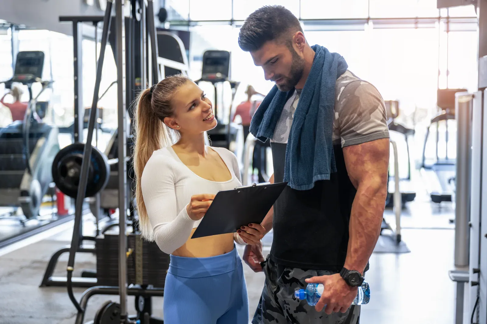 Trainer showing a clipboard program to a client beside gym machines