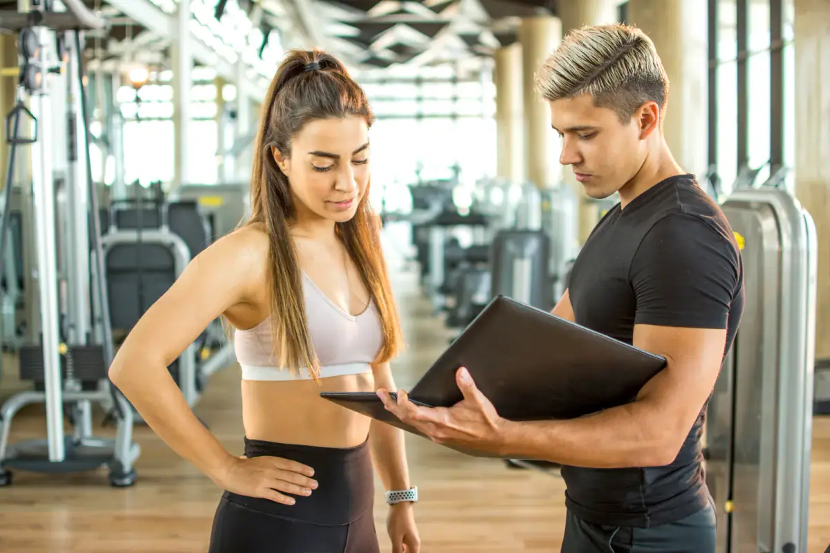 Personal trainer consulting a client over an open folder in a fitness facility