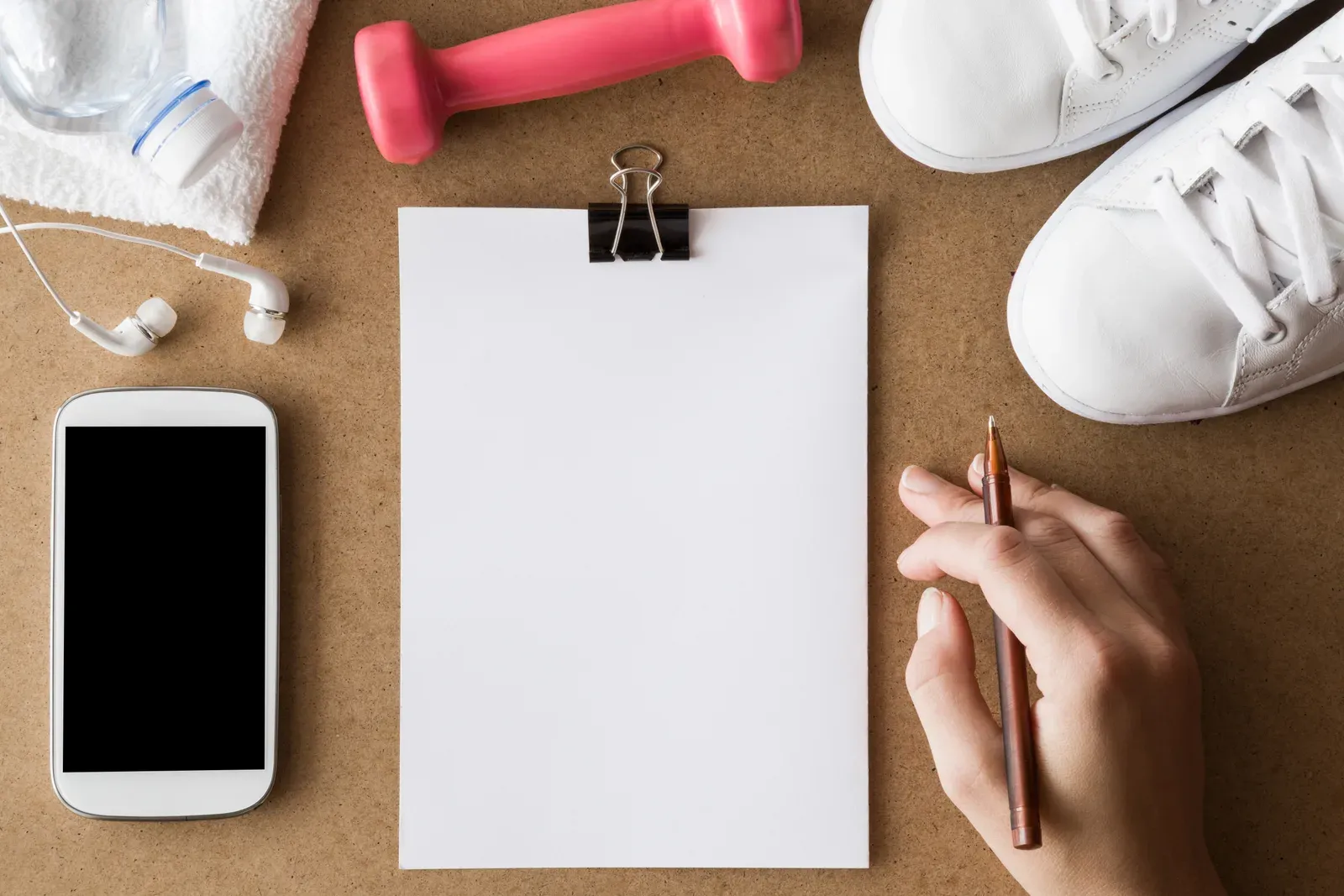 Flat lay of a blank workout notepad with a phone, dumbbell, and sneakers