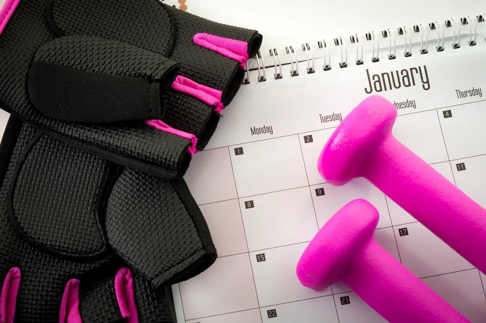 Workout gloves and small dumbbells resting on a January calendar page