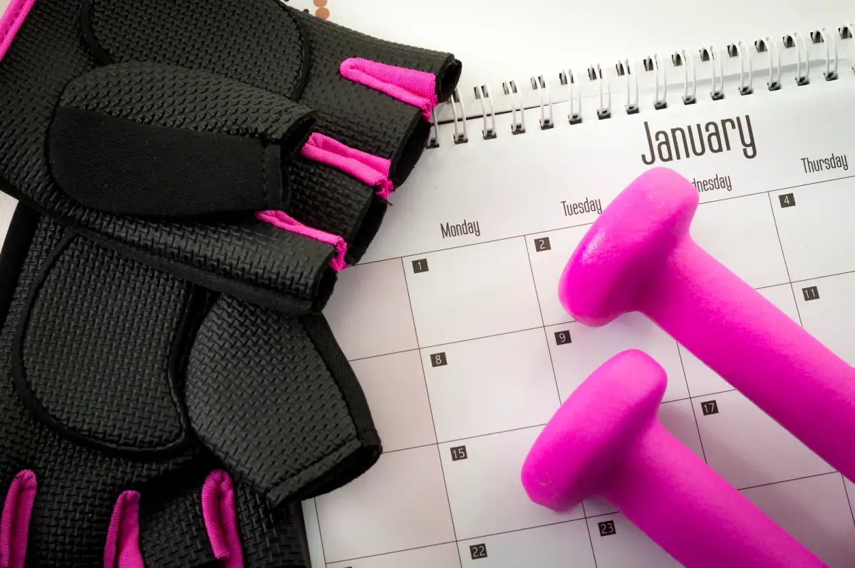 Workout gloves and small dumbbells resting on a January calendar page
