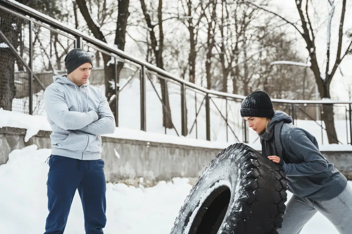 A trainer and a woman client working out with a tire on a cold, snowy day, relevant to winter outdoor personal training