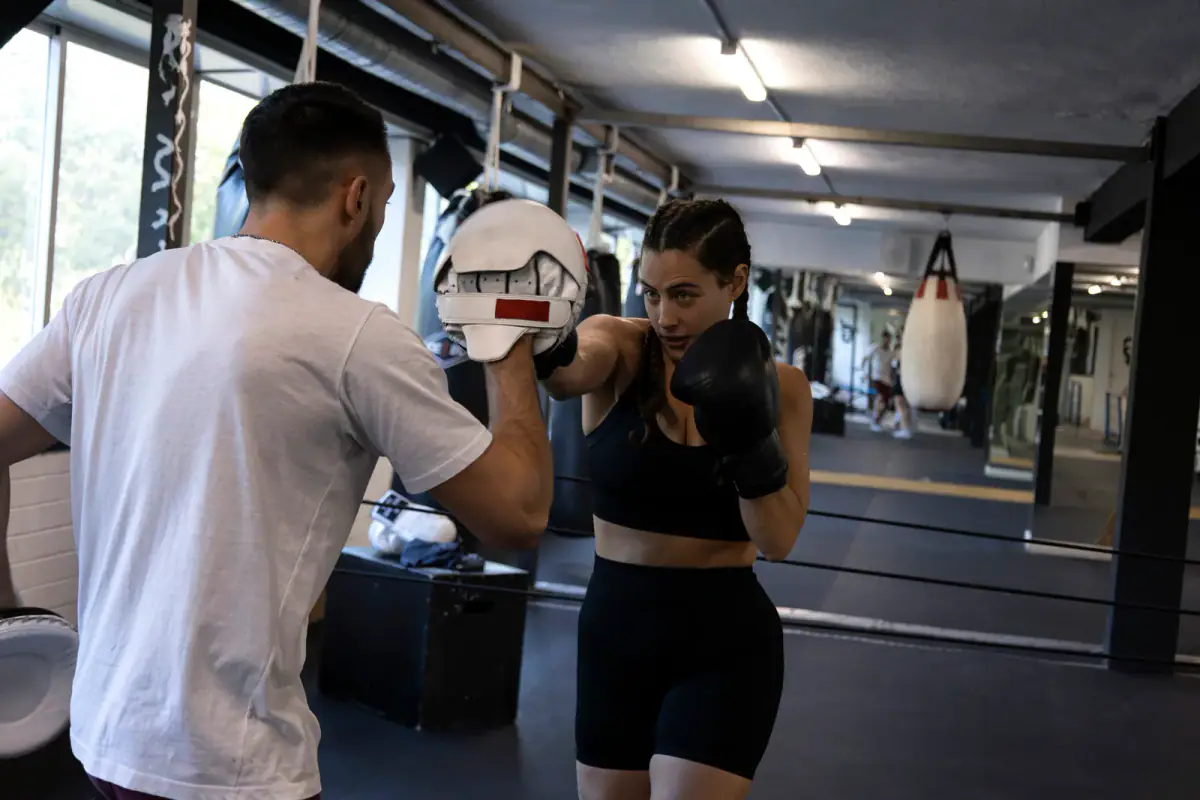 A woman practicing palm strikes on pads held by an instructor