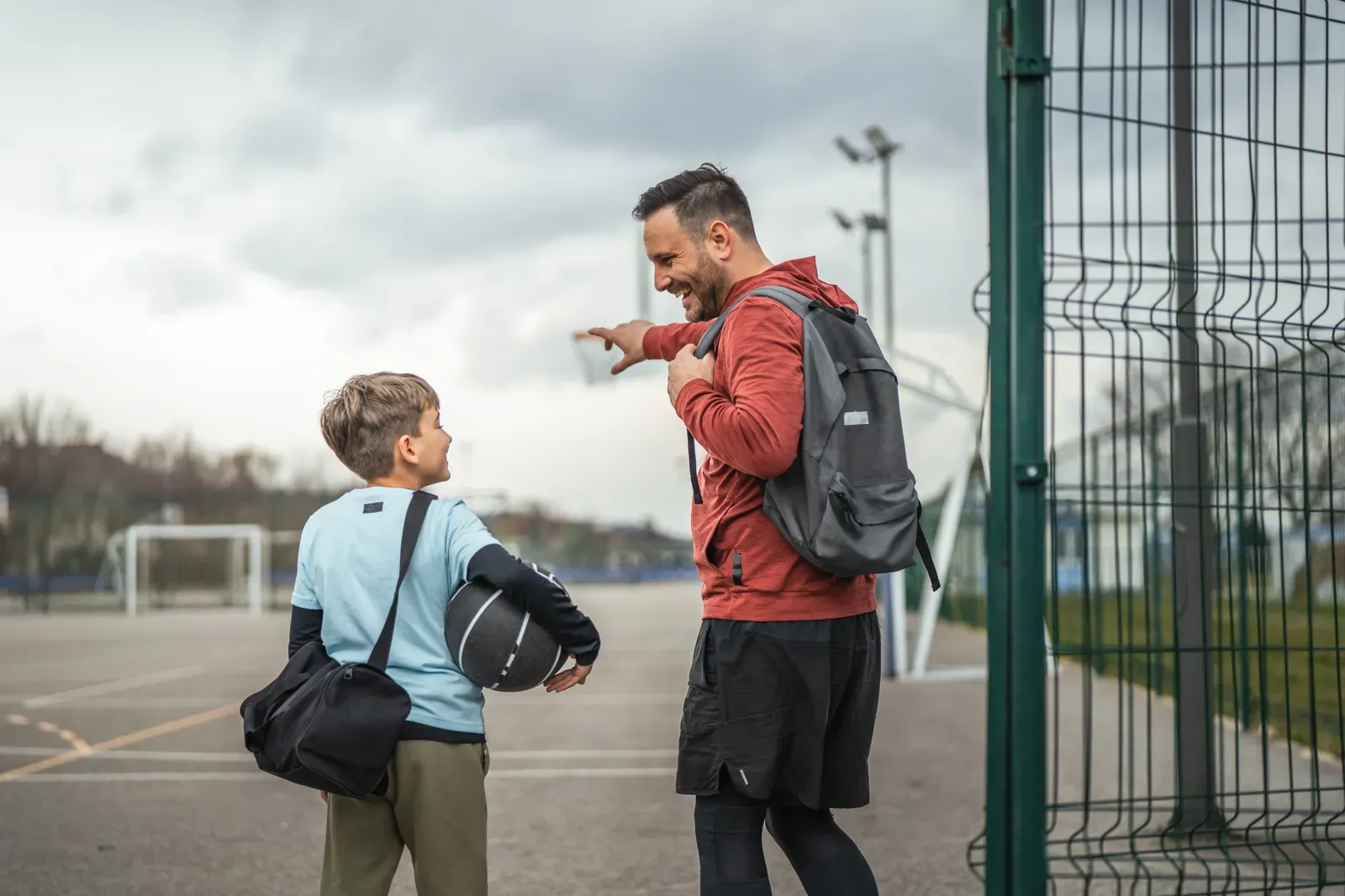 Parent with a packed gym bag waiting beside a sports field
