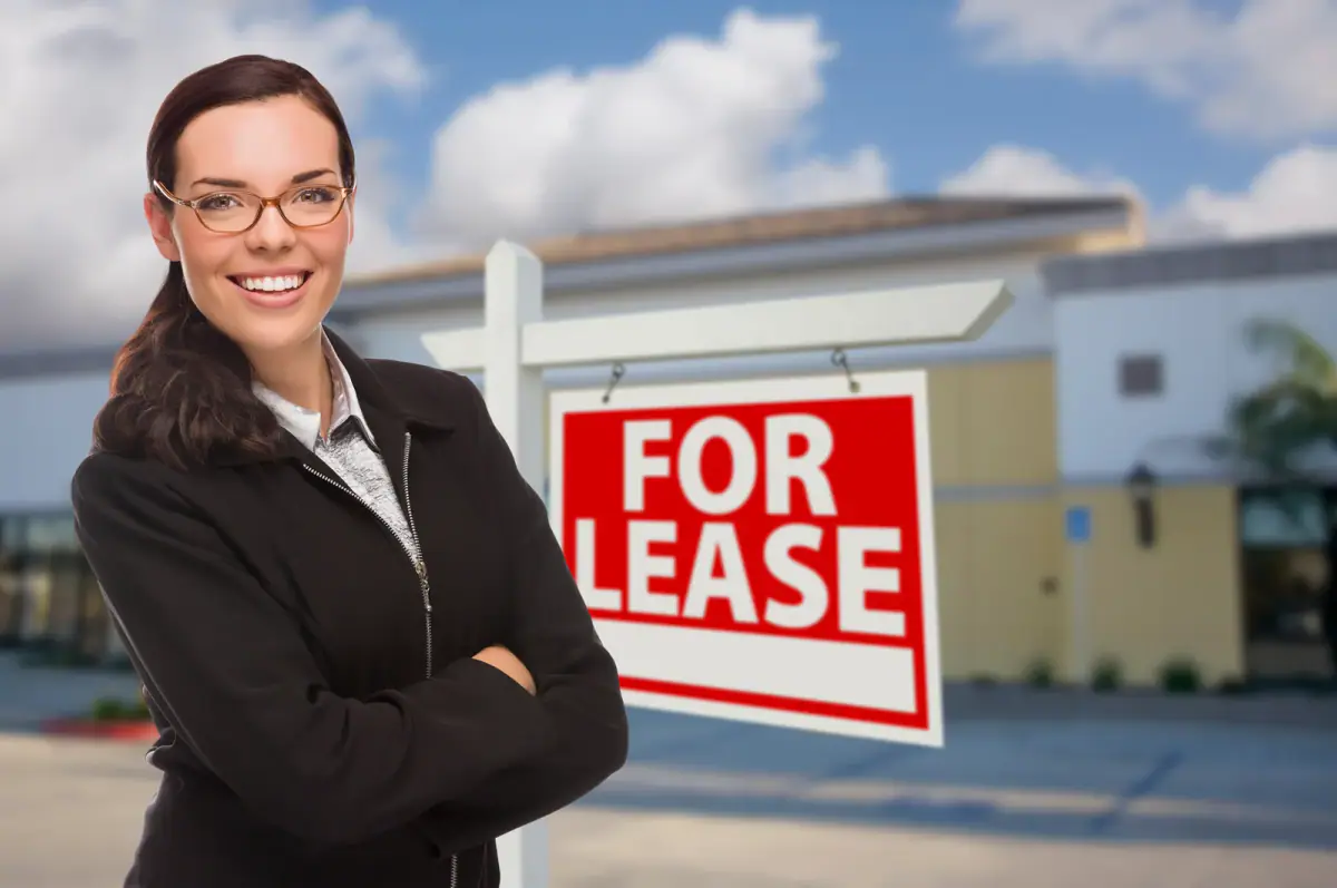 A woman in front of a commercial building with a for lease sign, relevant to zoning for a personal training studio